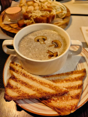 A creamy mushroom soup garnished with sliced mushrooms is served in a white bowl alongside two...