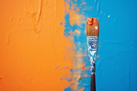 Paint brush dipped in orange paint on colorful orange and blue background, copy space. Home repair and finishing concept. AI generated.の素材