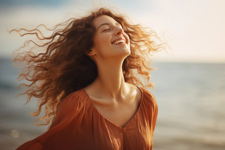 A woman with long, curly hair stands on a beach, her head tilted back as she smiles at the setting sun. Generative AI.の素材