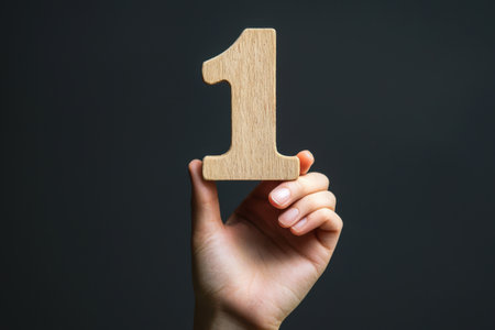 A hand displays a wooden number one sign, symbolizing first place or a beginning. The dark background enhances focus on the hand and sign, conveying a sense of achievement. Generative AIの素材