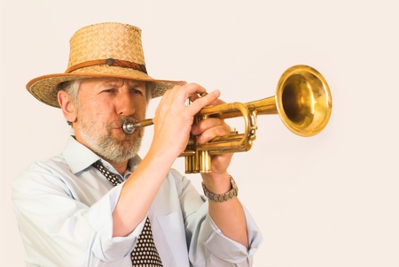 Horizontal image showing a matured, graying, unshaved trumpeter over 50 wearing a straw hut. His face is wrinkled, but happy, his eyes closed. He plays a brass trumpet. An effort visible on his face.の写真素材