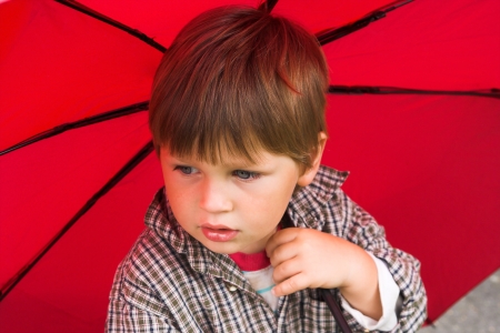 Little boy with a red umbrella in his hand is listening to the rain  His face collected の写真素材