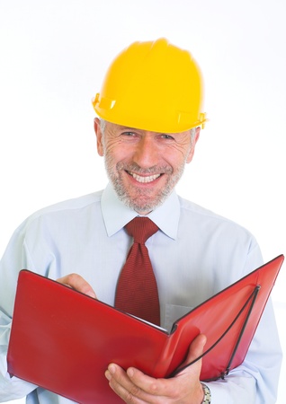 Vertical image presents graying white man, wearing yellow helmet, blue shirt and tie, who stands, laughing, with a folder of papers in his hands.の写真素材