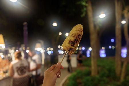 Handing the corn grill and bokeh backgroundの写真素材