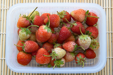 The pile of fresh strawberry in the plastic crate,Wooden tray backgroundの写真素材