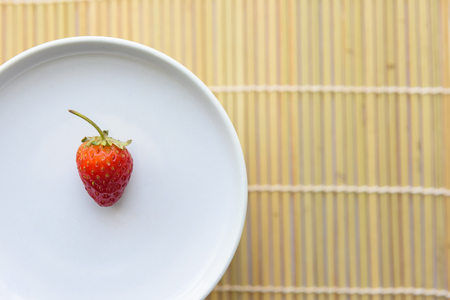 Single fresh strawberry on the white dish,Wooden texture backgroundの写真素材