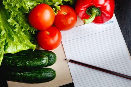 Fresh vegetables on the table: red pepper, lettuce, cucumber, tomatoes, sheet for notes - notepad. Cutting boardの写真素材