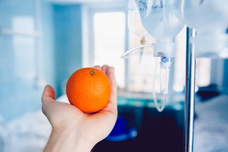 doctor's hand holds the orange against the dropper. Concept of the treatment of oranges with vitamin C - the replacement of fruit instead of pricks.の写真素材