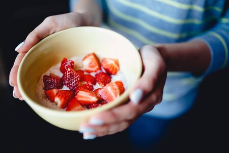 girl is holding a cup of porridge and chopped fresh strawberries. The concept is a healthy and nutritious breakfast for athletes.の写真素材