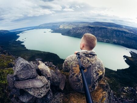 tourist man stands and sits in the mountains and rocks against the background of the sea. Mountains of Khibiny, Seydozero. Murmansk Region, Kola Peninsula, Russia. action camの写真素材