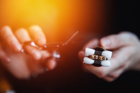 Vape.male master holds scissors, cotton wool and an electronic cigarette on a dark wood background.vaping deviceの写真素材