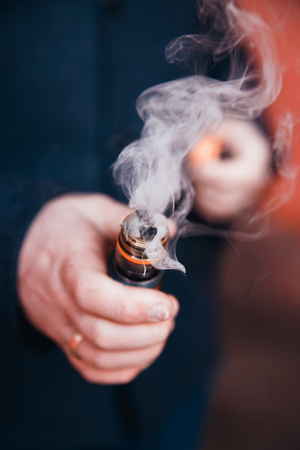 close-up of an electronic cigarette a vape is going to steam with a fragrant liquid on the fleece. The spiral is hot. The concept of replacement of cigarettes with tobacco, harmless smoking.の写真素材