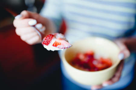 girl is holding a spoon with a strawberries cut with a knife in a bowl with a porridge on the milk, two halves. The concept of cooking a tasty, healthy, healthy breakfast with oatmeal.の写真素材