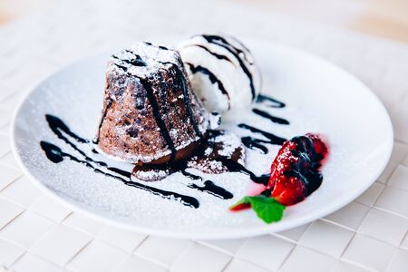 Chocolate fondant with strawberry fruit is served with an ice cream ball on a white plate.の写真素材
