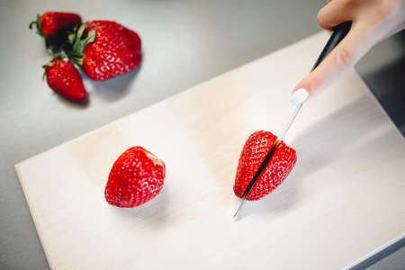 girl cuts a strawberry on a cutting board with a knife. The concept of preparing fruit slicedの写真素材