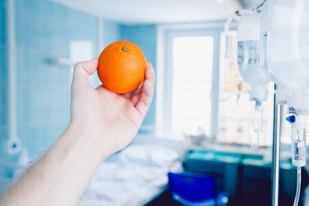 doctor's hand holds the orange against the dropper. Concept of the treatment of oranges with vitamin C - the replacement of fruit instead of pricks.の写真素材