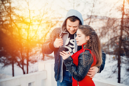 Vape guy and girl - lovers at sunset look in the phone and laugh. The concept of refusal of tobacco. の写真素材