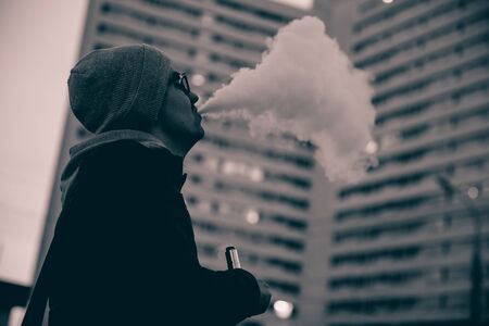 vaping man holding a mod device. cloud of vapor. Vape. high contrast and monochrome color tone.の写真素材