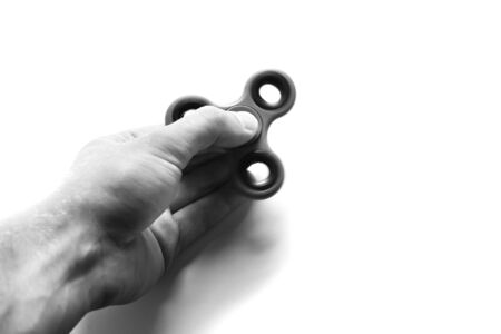 Hand holds Fidget finger spinner, anxiety relief toy on white isolated background, copyspace. Concept relieving stressの写真素材