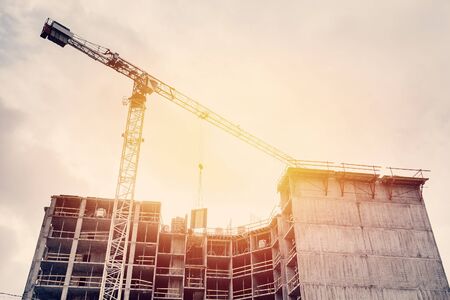 Large construction site including one cranes working on a building complex, with clear blue sky and the sun.の写真素材