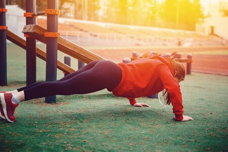 The girl on the sports field is squeezed out of the room. The concept of a healthy lifestyle and exercises for strengthening the hands and back.の写真素材