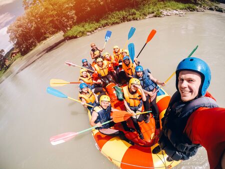 mountain Altai, RUSSIA - July 16, 2017: man in a helmet holds an action camera and makes selfie on the background of friends with oars, raftingのeditorial素材
