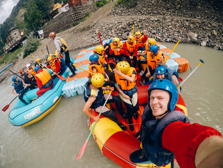 mountain Altai, RUSSIA - July 16, 2017: man in a helmet holds an action camera and makes selfie on the background of friends with oars, raftingのeditorial素材