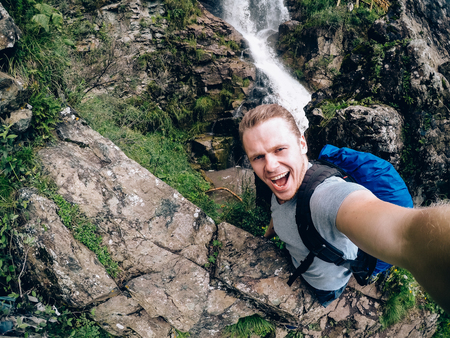 tourist man on a waterfall background holds an action camera and takes a picture of Selfie.の写真素材
