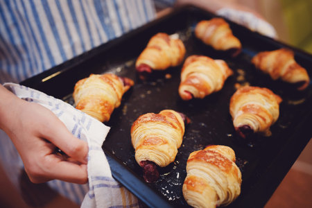 girl is holding a baking sheet with fresh croissants with a sweet, cherry filling.の写真素材