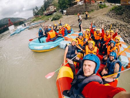 mountain Altai, RUSSIA - July 16, 2017: man in a helmet holds an action camera and makes selfie on the background of friends with oars, raftingのeditorial素材