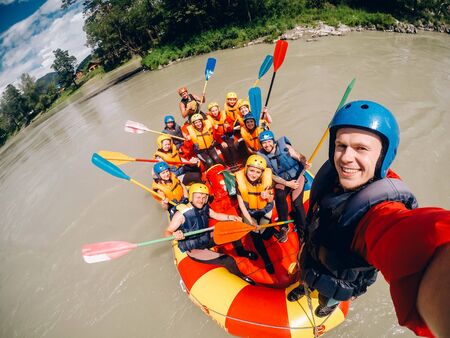 mountain Altai, RUSSIA - July 16, 2017: man in a helmet holds an action camera and makes selfie on the background of friends with oars, raftingのeditorial素材