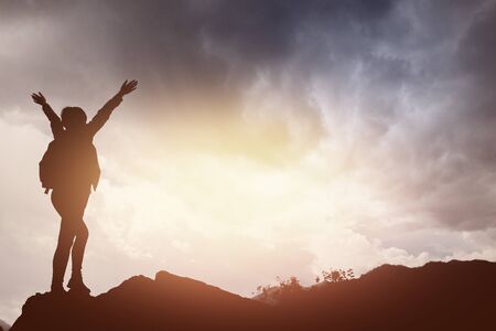 tourist girl stands on top of a mountain and has fun against backdrop of mountains and the river. setting sun. Concept to achieve the goal, go up, go to successの写真素材