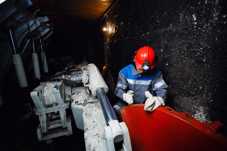 young miner man underground in a mine for coal mining in overalls is busy with work, repairing against the backdrop of mining equipment. Portrait.の写真素材