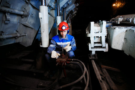 young coal miner is underground in mine for coal mining in overalls against backdrop of mining...