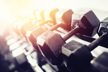 lot of dumbbells stand in row in the gym, glare of light. Concept slimming, musculature,...