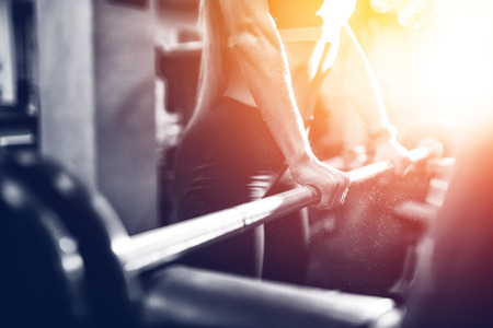 Close-up of a girl holding her hands with a barbell for pulling, squatting, fitness in the gym. Concept sports, toned picture, copyspace for text. Glare of sun and light.の写真素材