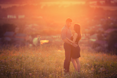 man and girl in love romantic lovers kissed, hugged sunset, sunrise against background of mountains and mist, sun, clouds in fiery red kiss, love, date.の写真素材