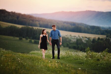 Lovers walk together on the road in the park against the backdrop of mountains, hills, fog, sunset. The concept of tender feelings between a guy and a girl, a look, feelings, love.の写真素材