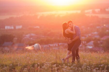 Lovers in mountains against background of fog and hills, a crimson, scarlet, red, orange sunset, sun shines in back, backlight, glare of sun. concept of first love and kiss of tender romanticの写真素材