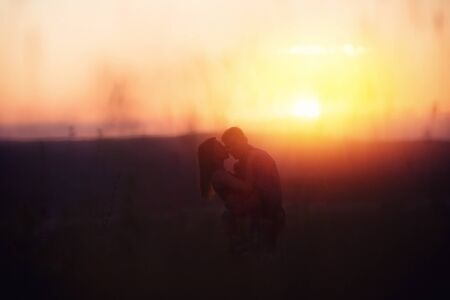 Man and girl lovers in love romantic date kissing, hugging sunset, sunrise against  background of mountains and fog, the sun, clouds in fiery red, orange colors. concept of wedding, first kiss, love, dateの写真素材