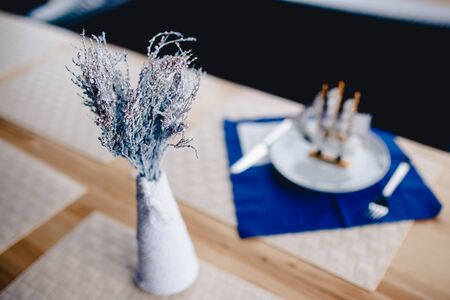 Dry flowers painted in white are in a vase on a wooden table, the breadboard model of a wooden ship is a model of a sailboat. Concept detail of the interior of the restaurant and cafe.の写真素材