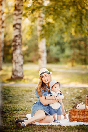 Ideal family: mother and baby son sitting in the park on the grass playing with rabbits. Concept childhood, animals and people are best friends, home pets.の写真素材