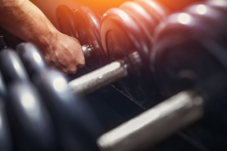 Close-up of a man takes a dumbbell in the gym. sun lightの写真素材