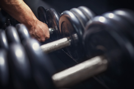Close-up of a man takes a dumbbell in the gym.の写真素材