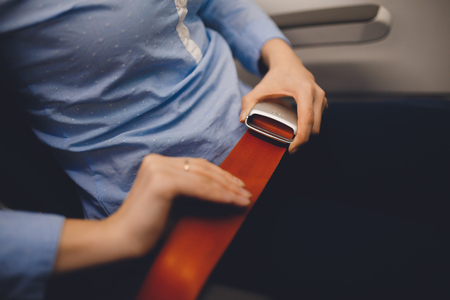 Girl passenger fastening seat while belt sitting on airplaneの写真素材