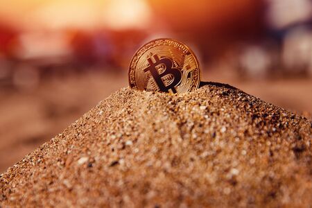 Bitcoin on golden sand, in background sun lightの写真素材
