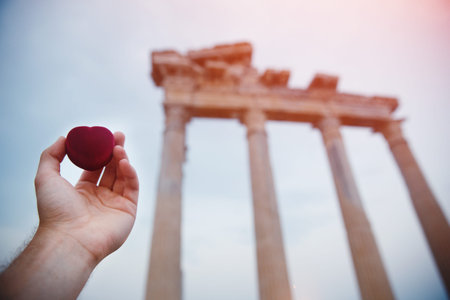 Hand of man with wedding ring and gift box against the background of the ancient ruins of the temple of Apolloの写真素材