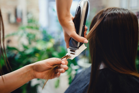 Master performs polishing of split ends of hair for client of girl in hairdresser. concept of hair care, healthy hair.の写真素材