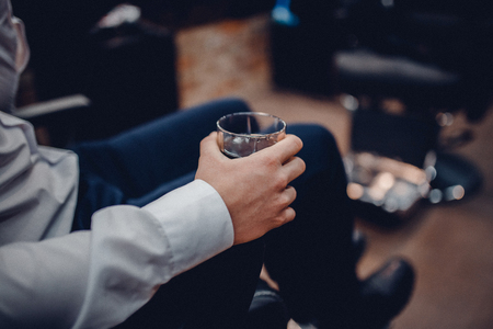 man is holding a glass of whiskey in the barber's chair in barbershopの写真素材