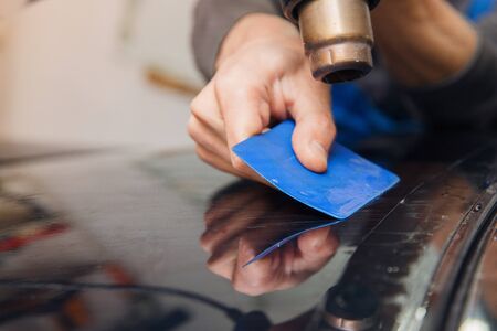 Master installs a tint film for the car glass with a hairdryer and spatula with glare of light. Concept tinting carの写真素材